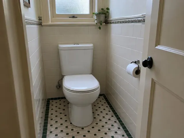 Clean white toilet in a tiled small bathroom with a window and patterned floor in Lane Cove