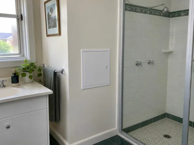 Bathroom wall with a small access panel beside a tiled shower and vanity in Lane Cove